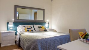 A neatly arranged bedroom with a bed, bedside tables, a mirror, and a desk with a chair. - Vrbo Property (Volterra)