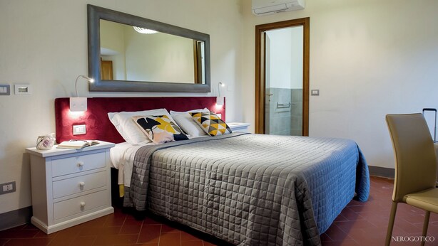 A bedroom with a bed, bedside table, lamp, mirror, and an air conditioning unit. - Vrbo Property (Volterra)