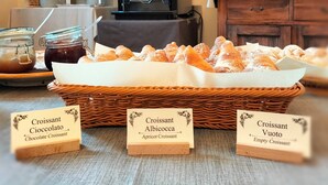 A bakery display with labeled croissants and a coffee machine in the background. - Vrbo Property (Volterra)