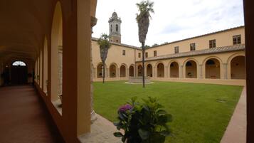 Un cortile con una fontana al centro, circondato da archi e un edificio con una torre sullo sfondo.