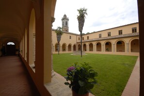 A courtyard with a central fountain, surrounded by arches and a building with a tower in the background.
