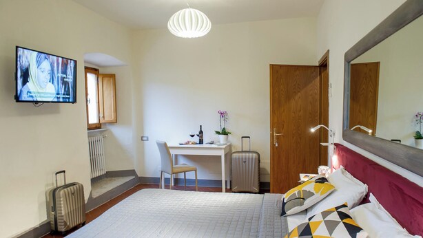A hotel room with a bed, a desk, a chair, a television, a suitcase, and a mirror.