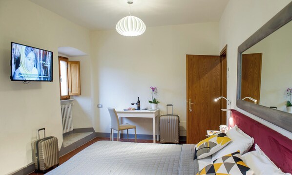 A hotel room with a bed, a desk, a chair, a television, a suitcase, and a mirror. - Just a stone's throw from Volterra: rooms with all the comforts (Volterra)