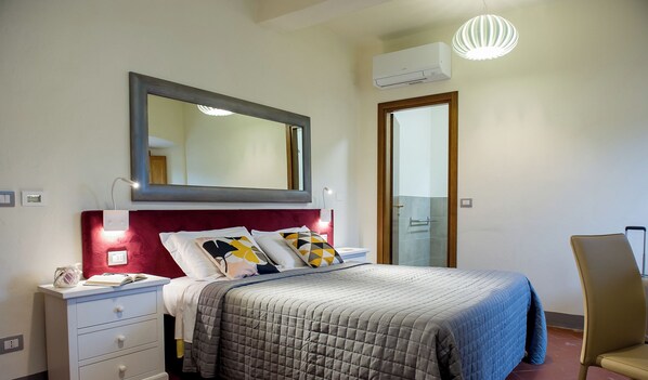 A bedroom with a bed, bedside table, lamp, mirror, and an air conditioning unit. - Vrbo Property (Volterra)