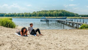 Una playa arenosa con una pareja relajándose, un muelle y un barco al fondo.