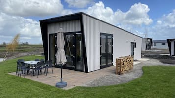 En moderne bygning med en terrasse, udendørs møbler og en stabel brænde.