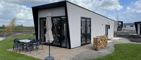 A modern building with a patio area, outdoor seating, and a stack of firewood.
