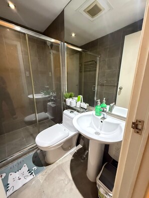 A modern bathroom with a glass-enclosed shower, a toilet, a sink, and a mirror. - Stylish Studio with Stunning Makati City Views at Gramercy Residences Makati. (Makati)