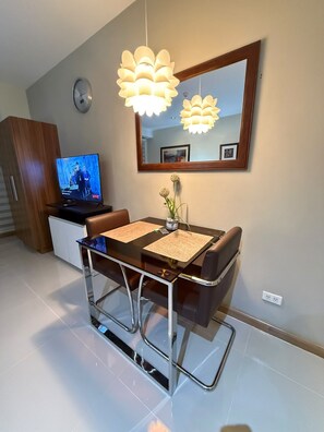 A modern dining area with a glass table, leather chairs, and a television on a cabinet. - Stylish Studio with Stunning Makati City Views at Gramercy Residences Makati. (Makati)