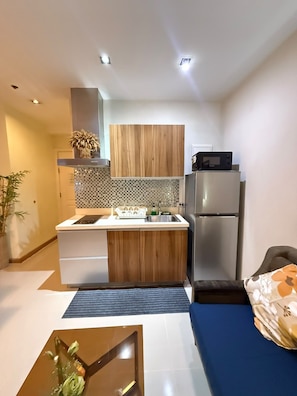 A compact kitchen with wooden cabinets, a stainless steel refrigerator, and a microwave. - Stylish Studio with Stunning Makati City Views at Gramercy Residences Makati. (Makati)