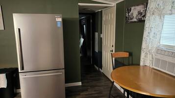 A compact kitchen with a refrigerator, a dining table with chairs, and a hallway leading to another room.