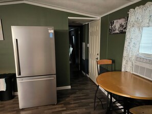 A compact kitchen with a refrigerator, a dining table with chairs, and a hallway leading to another room.