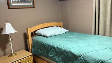 A bedroom with a single bed, a bedside table with a lamp, a framed picture on the wall, and an air conditioning unit.