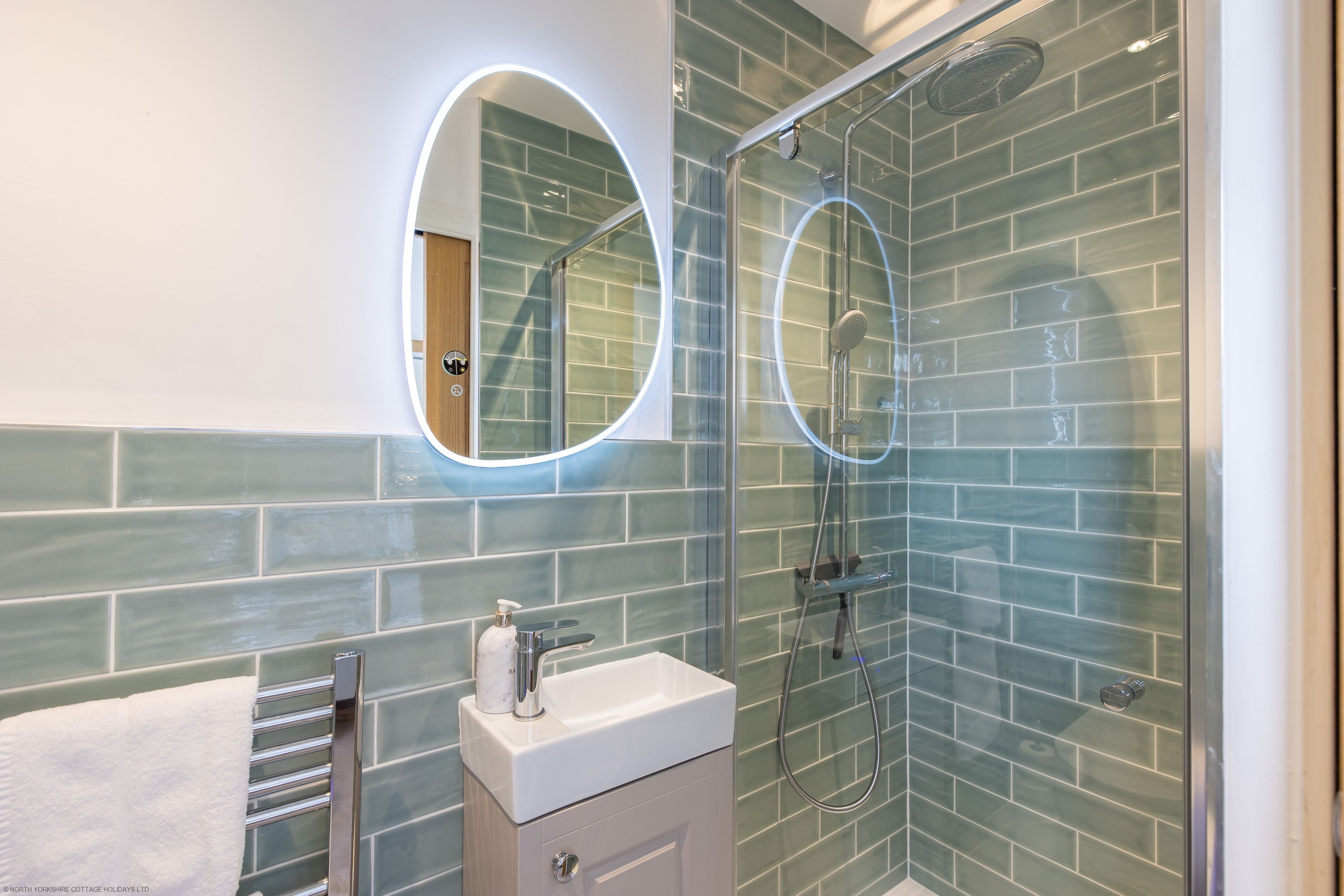 Un bagno con cabina doccia in vetro, lavabo con piano in marmo e specchio a cornice circolare.
