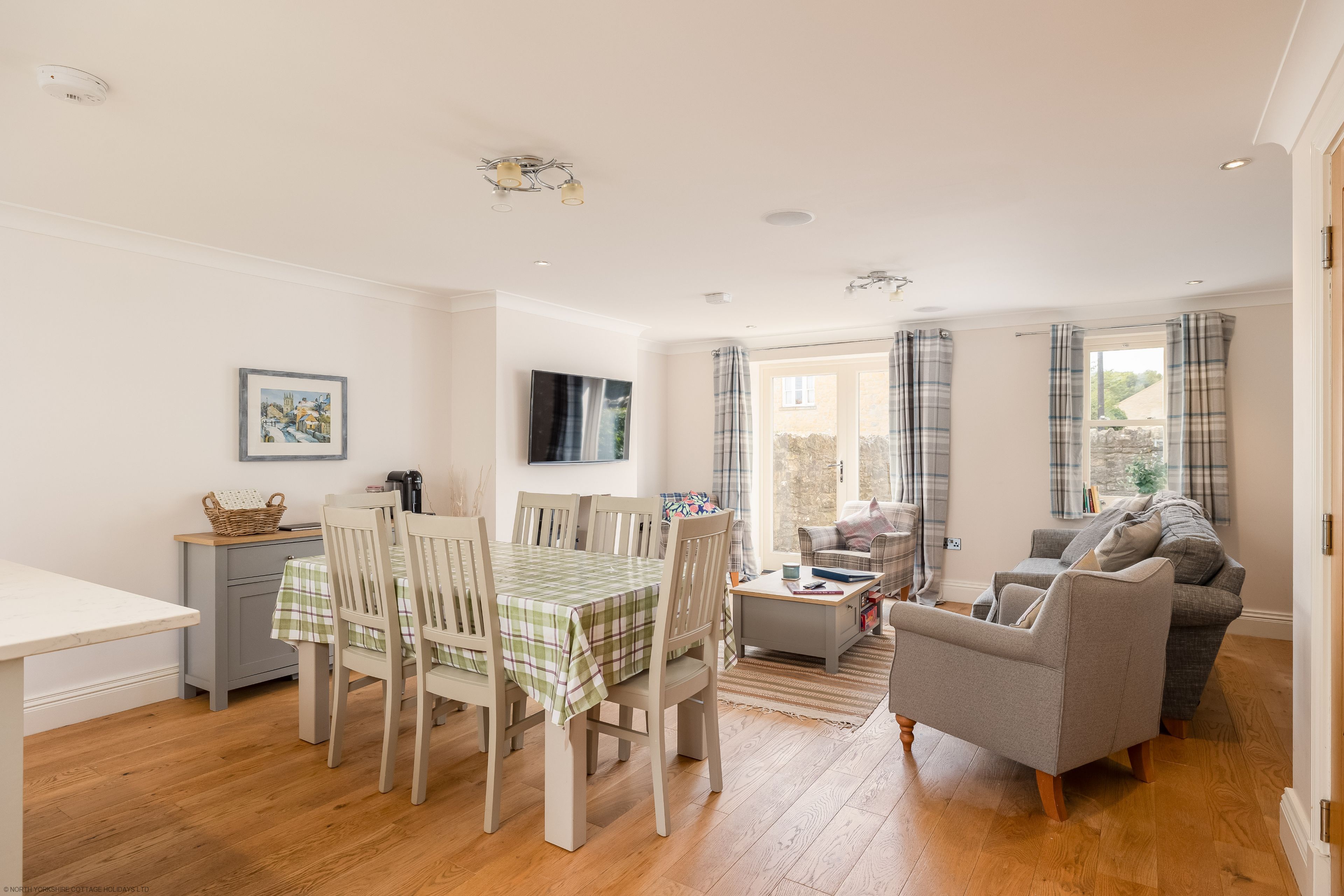 A well-lit, open-plan living space with a dining area, a sofa, and a television.