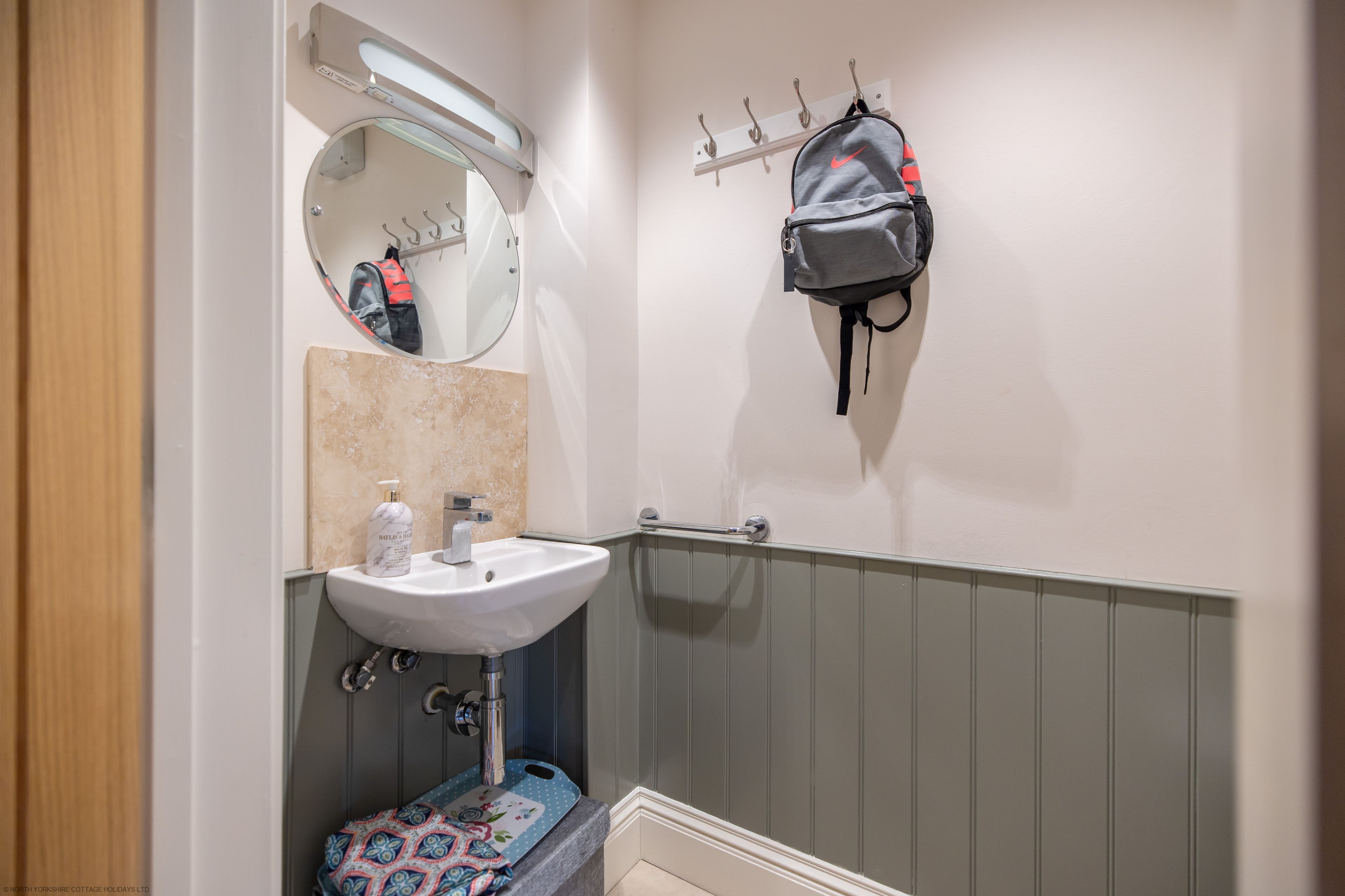 A bathroom with a sink, mirror, towel rack, and a hanging backpack.
