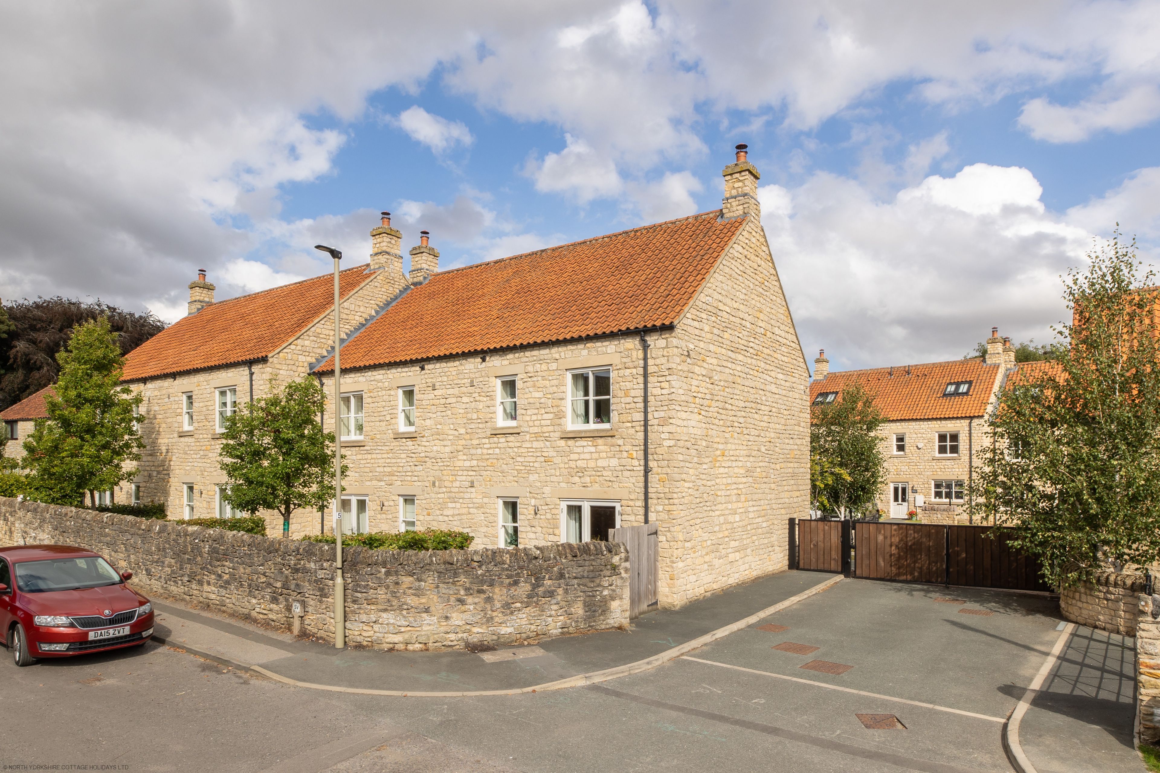 A stone building with a red-tiled roof, a paved driveway, and a parked car.