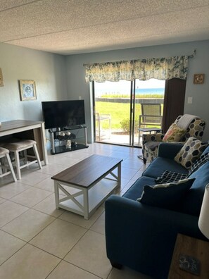 A living room with a sofa, a coffee table, a TV, and a dining area with chairs. - Cozy Ocean & Pool View 2-Bedroom, 2-Bathroom Condo in Amazing Ormond Beach Fla. (Ormond Beach)