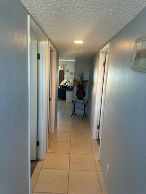 A hallway with a tiled floor leading to a living area with a couch and a table with a vase. - Cozy Ocean & Pool View 2-Bedroom, 2-Bathroom Condo in Amazing Ormond Beach Fla. (Ormond Beach)