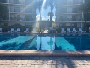 A swimming pool with lounge chairs and palm trees in the background. - Cozy Ocean & Pool View 2-Bedroom, 2-Bathroom Condo in Amazing Ormond Beach Fla. (Ormond Beach)