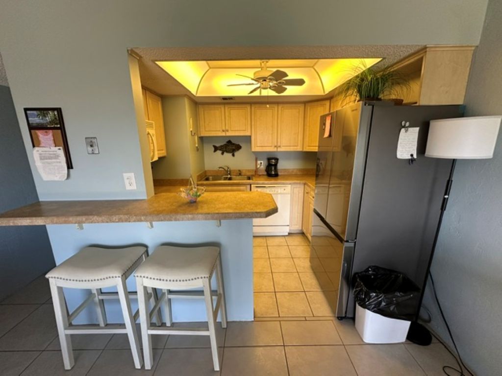 Una cocina con una isla central, dos taburetes de bar, un refrigerador y un ventilador de techo.