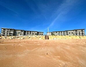 A beachfront hotel with multiple floors, a sandy beach in the foreground, and a clear blue sky. - Cozy Ocean & Pool View 2-Bedroom, 2-Bathroom Condo in Amazing Ormond Beach Fla. (Ormond Beach)