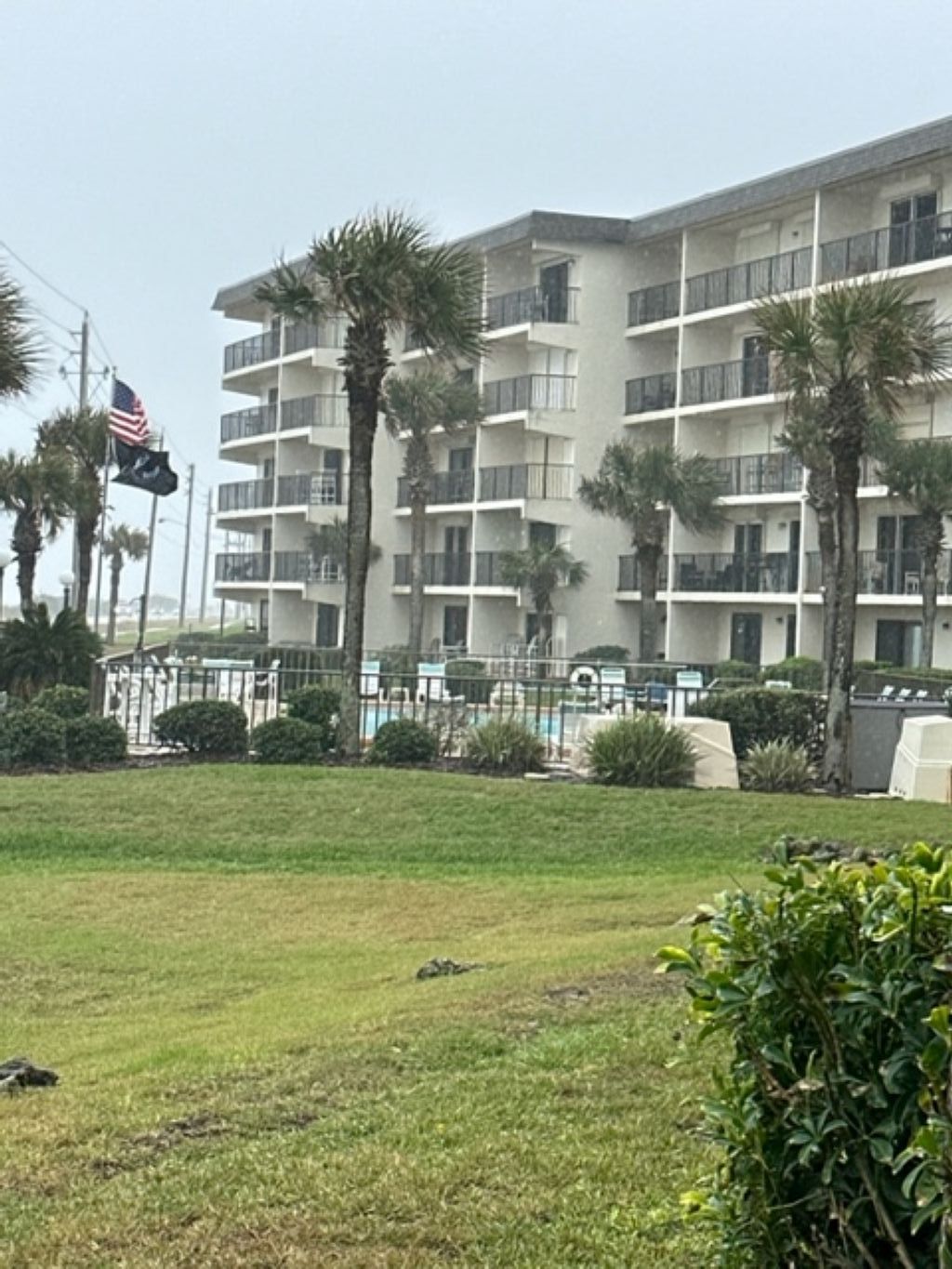 A multi-story hotel with balconies, surrounded by palm trees and a grassy area.