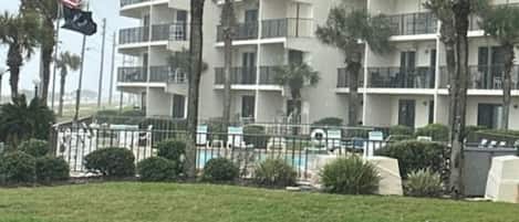 A multi-story hotel with balconies, surrounded by palm trees and a grassy area.