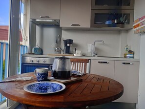 Eine kleine Küche mit Herd, Kaffeemaschine und Spüle. Ein Holztisch steht bereit, mit Tellern und einem Wasserkocher.