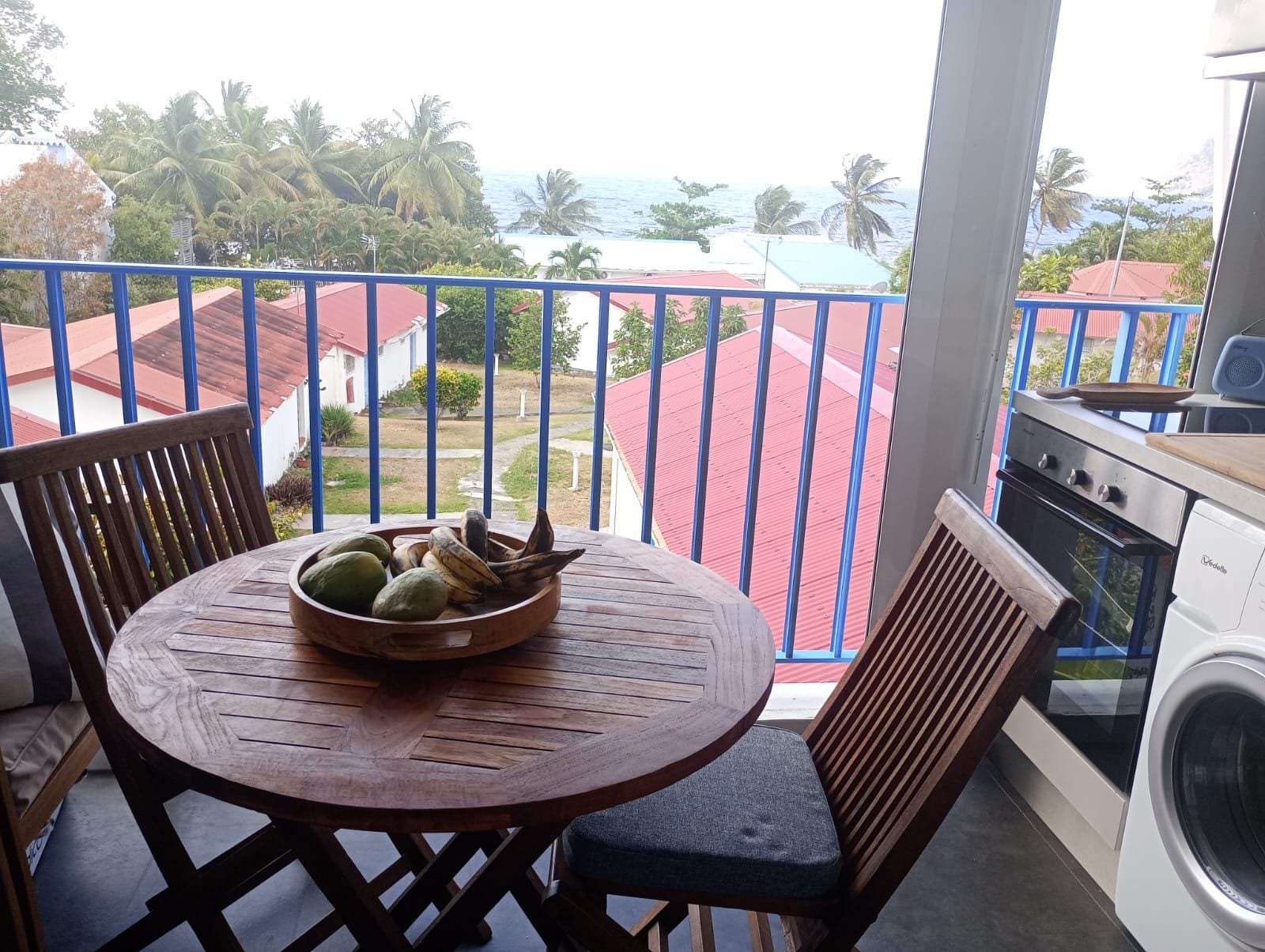 Ein Balkon mit Blick auf das Meer, ein Tisch mit Obstschale und eine Waschmaschine.
