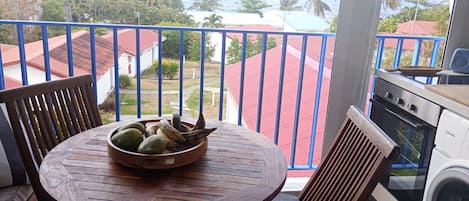 A balcony with a view of the ocean, a table with a bowl of fruit, and a washing machine.