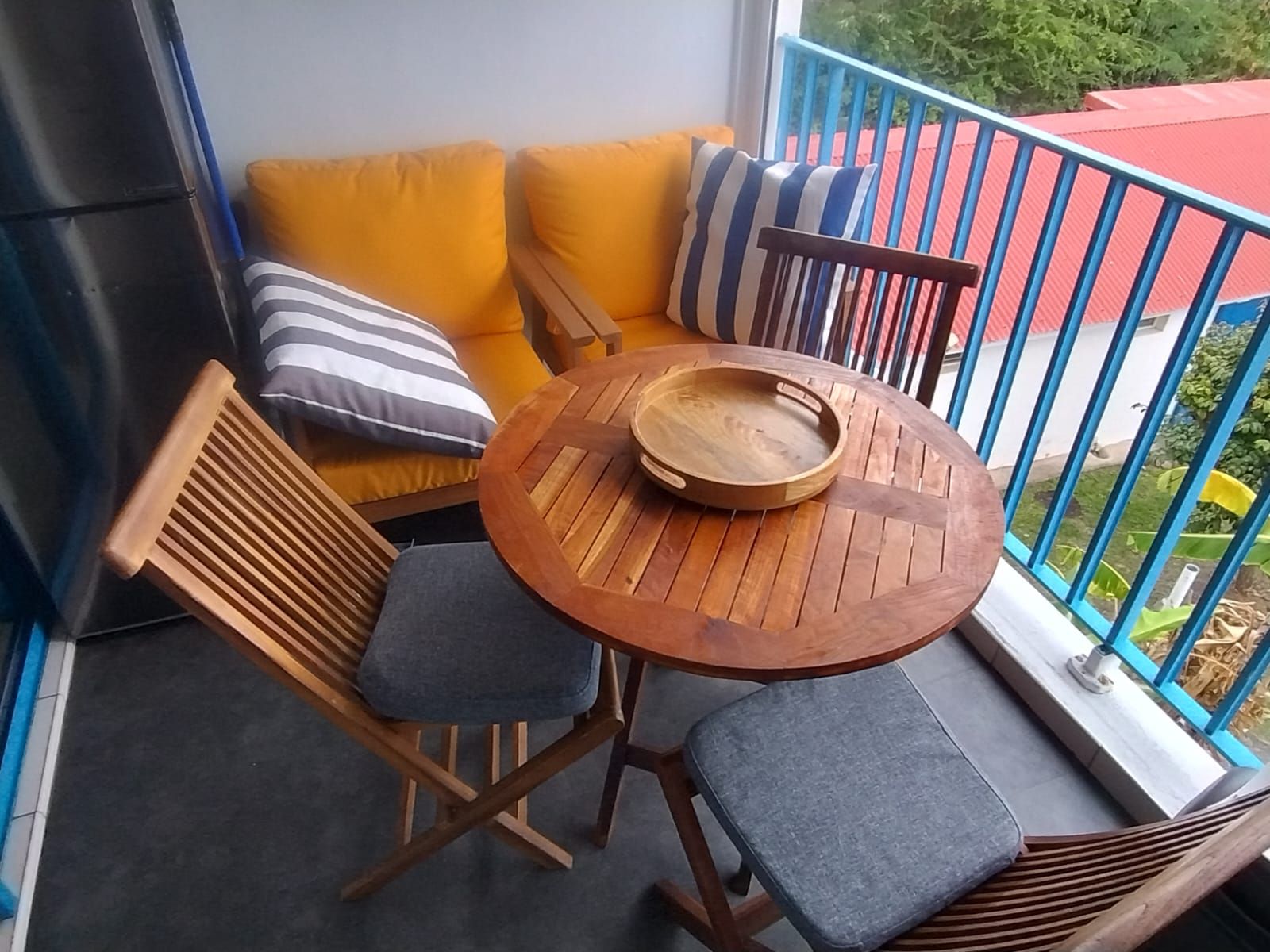 A balcony with a wooden table, two chairs, and a sofa with cushions.