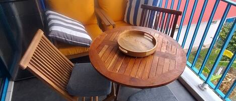 A balcony with a wooden table, two chairs, and a sofa with cushions.
