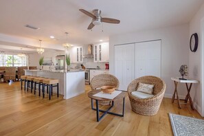 A spacious living area with a dining set, wicker chairs, a central table, and a kitchen in the background. - Sea Swept Mermaid: Canal-front with pool and kayaks (Anna Maria)