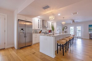 A modern kitchen with a central island, stainless steel appliances, and a dining area with bar stools. - Sea Swept Mermaid: Canal-front with pool and kayaks (Anna Maria)