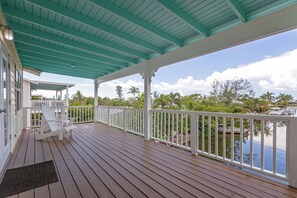 A covered wooden deck with white railings, a bench, and a view of a water body with boats. - Sea Swept Mermaid: Canal-front with pool and kayaks (Anna Maria)
