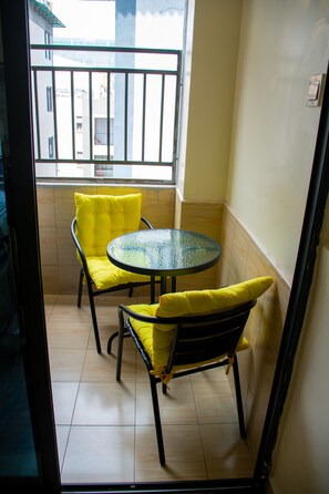 A small balcony with a glass table and two chairs, each with a yellow cushion. - Kileleshwa Gem|Luxury 2b near Westlands (Nairobi)