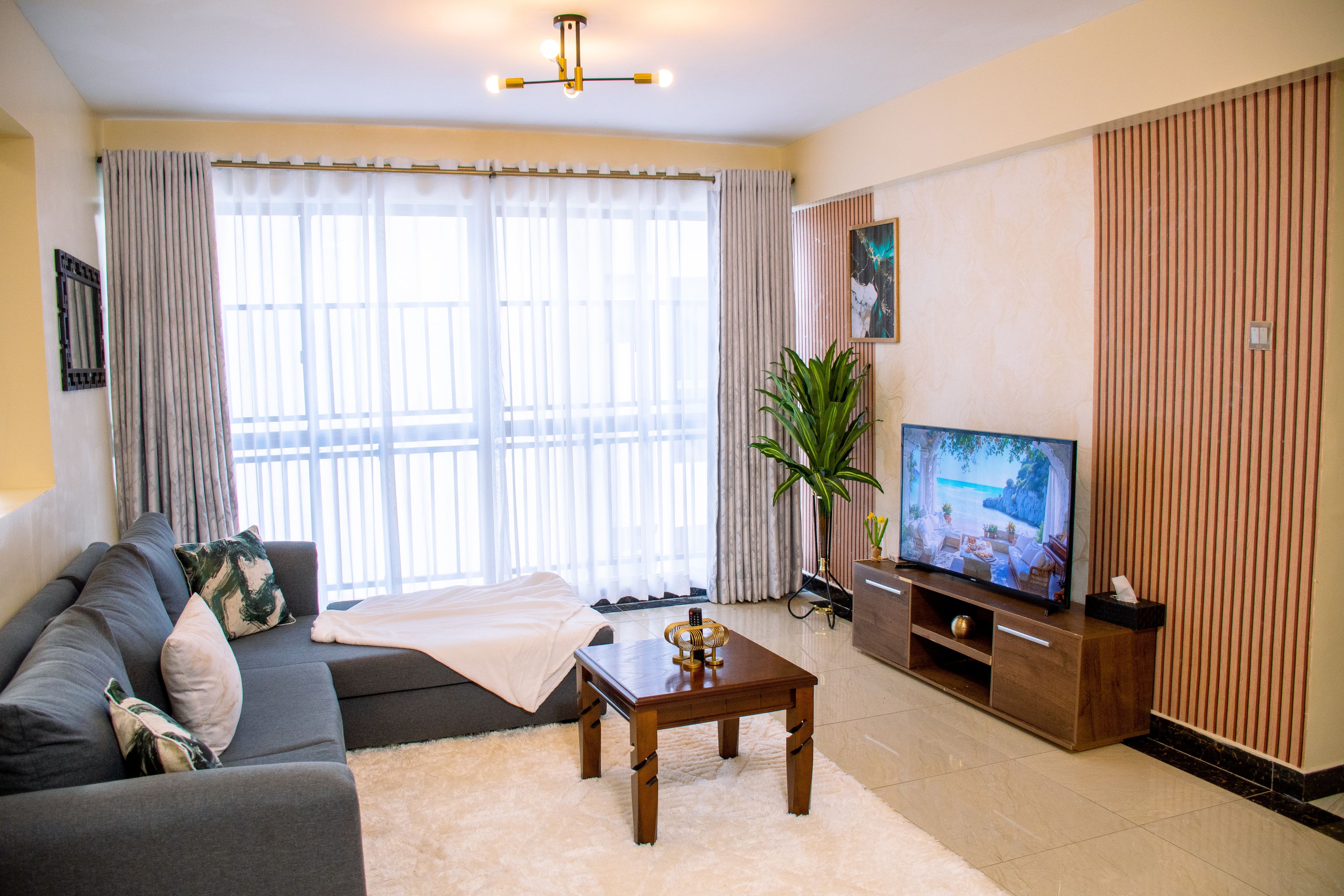 A living room with a sofa, a coffee table, a TV, and a large window with curtains.