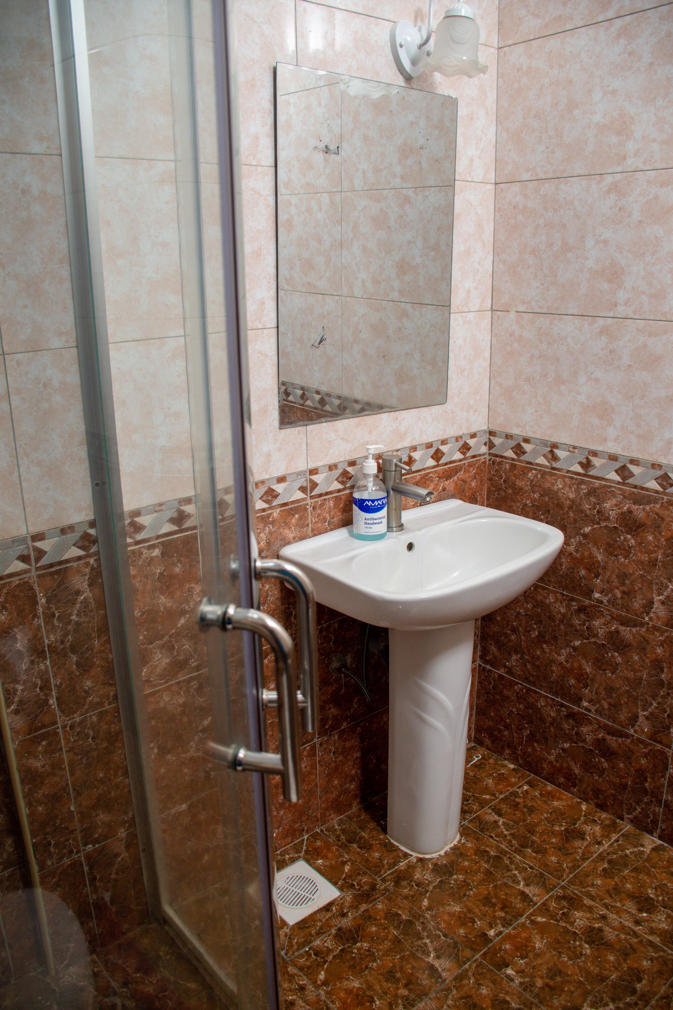 Un baño con cabina de ducha de vidrio, un lavabo con dispensador de jabón y un espejo sobre el lavabo.