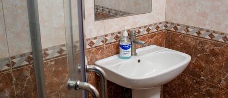 Un baño con cabina de ducha de vidrio, un lavabo con dispensador de jabón y un espejo sobre el lavabo.