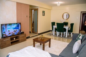 Ein Wohnzimmer mit Fernseher, einer Couch, einem Couchtisch und einem Essbereich mit Stühlen und einem Tisch.