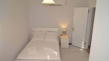 Una cama bien hecha con almohadas y una toalla doblada, una lámpara de noche y una puerta a la derecha.
