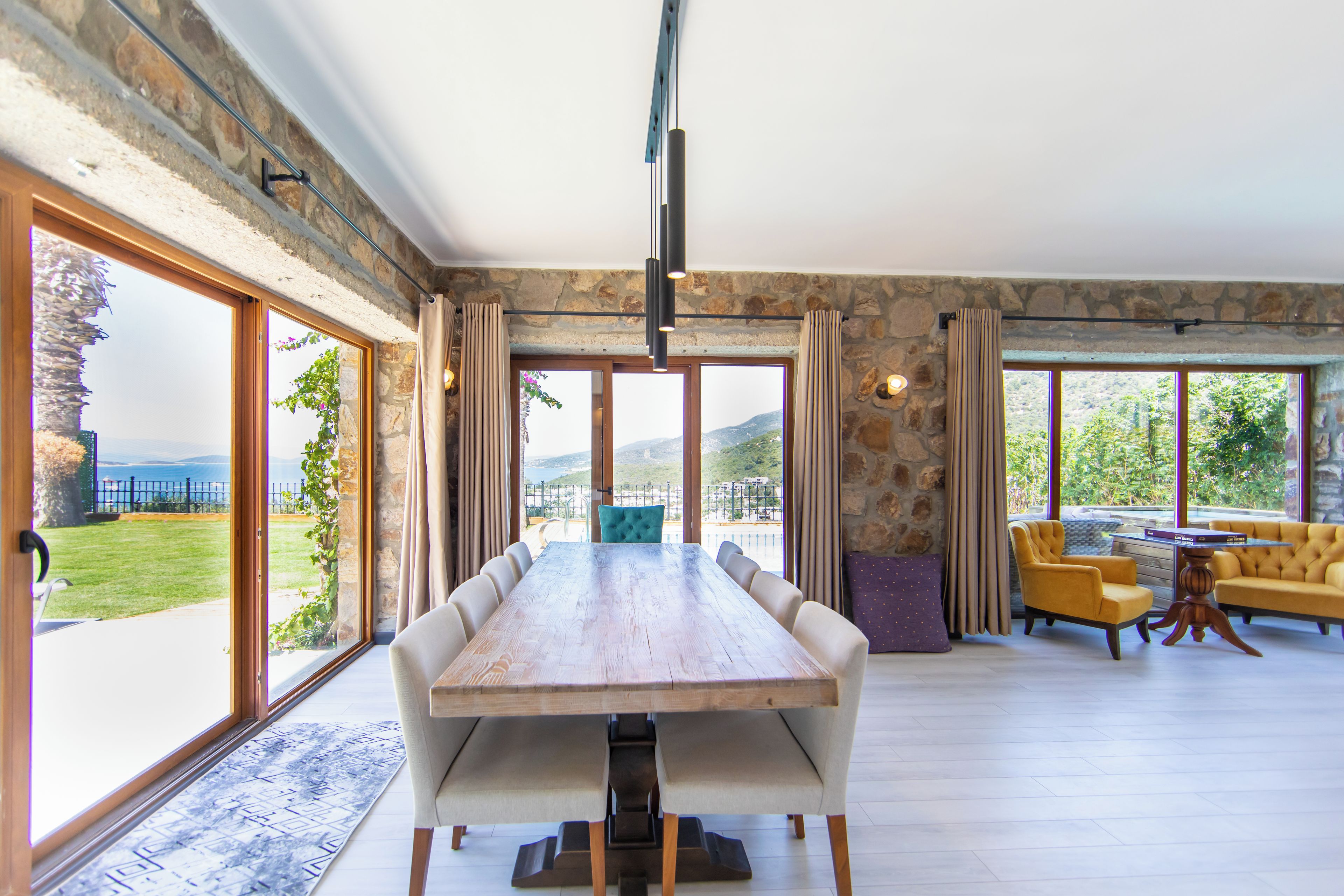 Un comedor amplio con una gran mesa de madera, varias sillas y vistas al exterior a través de amplios ventanales.