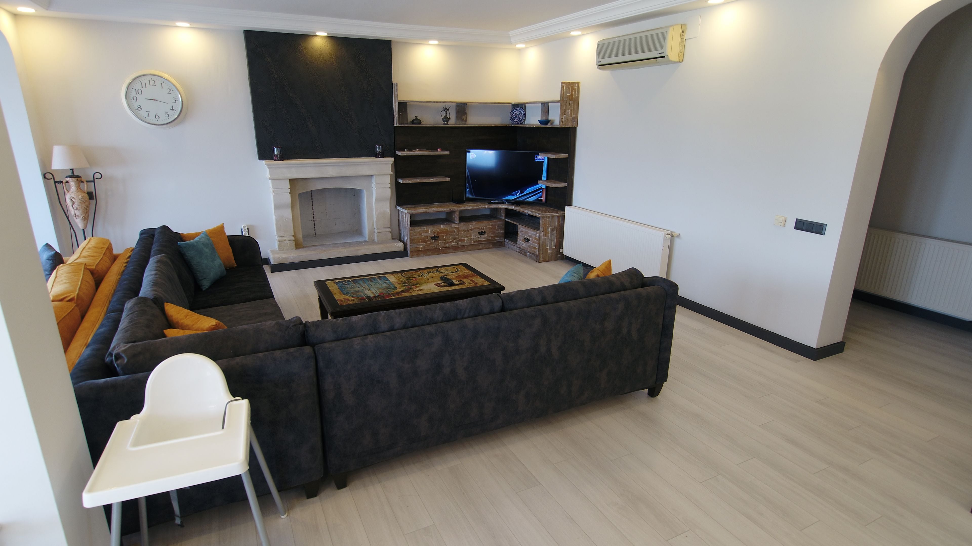 A modern living room with a sectional sofa, a fireplace, a flat-screen TV, and a dining area.