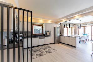 A modern kitchen with white cabinets, a built-in oven, and a large island with bar stools. - Mira Premium Villa (Torba)