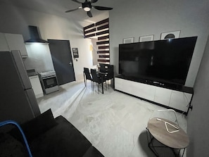 Eine moderne Küche mit Herd, Kühlschrank und Essbereich inklusive Stühle und Fernseher.