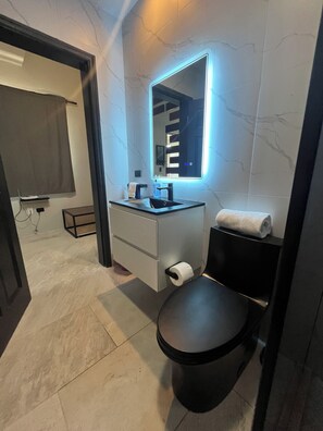 Ein modernes Badezimmer mit einer schwarzen Toilette, einem weißen Waschtisch mit Spiegel und einem Handtuch an der Wand.