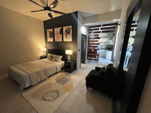 Een moderne slaapkamer met een bed, nachtkastjes, een plafondventilator en uitzicht op de keuken.