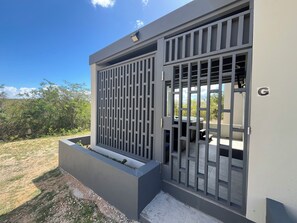 A modern building with a gated entrance, a small outdoor seating area, and a view of the surrounding landscape. - Cozy 1-bedroom studio in serene The Valley with AC and gym (The Valley)