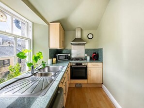 A compact kitchen with a sink, microwave, stove, and wooden cabinets. - Cozy 1BR in New Town - Steps from the Royal Mile (Edinburgh)